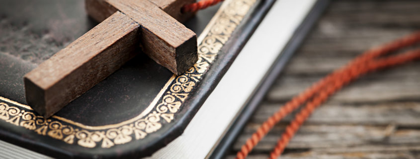 Closeup of simple wooden Christian cross necklace on holy Bible